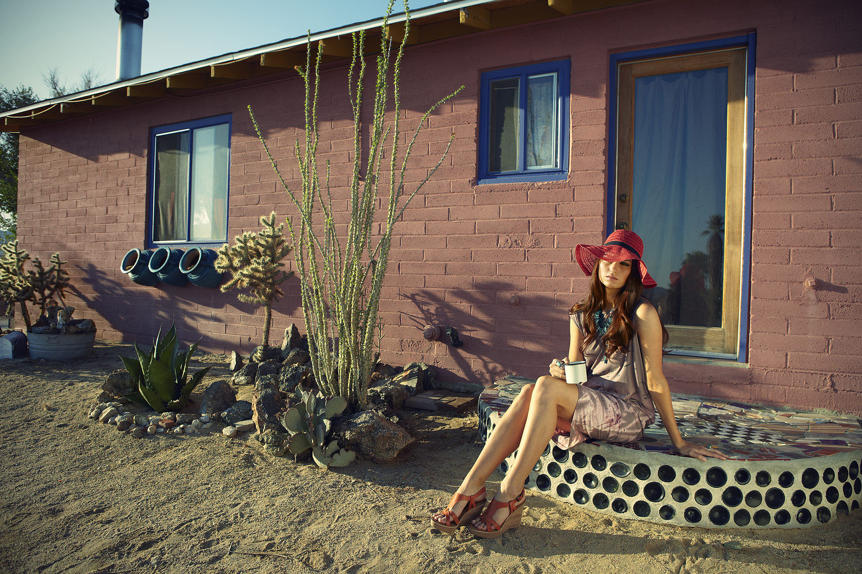 Red headed woman sitting on stoop with red floppy hat in front of pink house