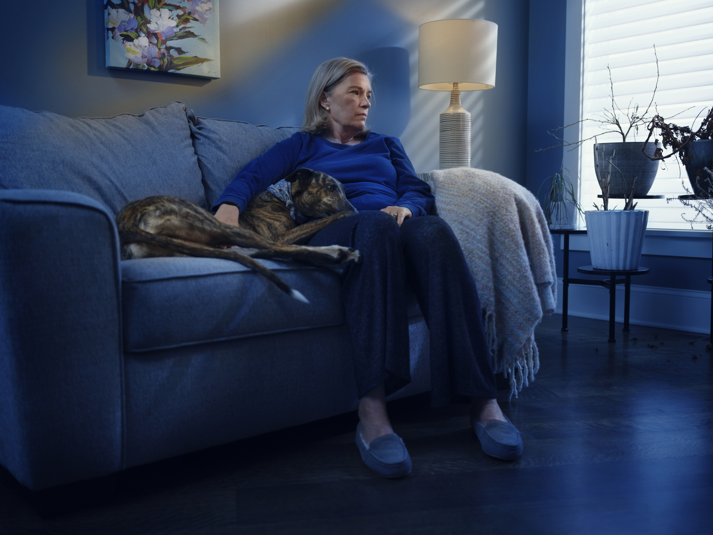 Depressed senior woman sitting with greyhound on couch
